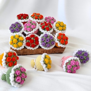 Pode incluir: Uma coleção de buquês de flores de crochê em várias cores, incluindo vermelho, amarelo, roxo e rosa. Os buquês estão dispostos em uma cesta e são feitos com uma borda de crochê branca.