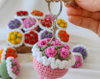 Puede incluir: Un llavero de flores de crochet rosa con un borde blanco de crochet y hojas verdes. El llavero está unido a un anillo y una cadena plateados.