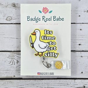 May include: A yellow and white badge reel with a cartoon goose holding a knife and the text "It's time to get silly". The badge reel has a gold glitter charm.