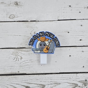 May include: A white plastic badge holder with a blue and white cartoon image of a person wearing a cowboy hat and holding a guitar. The text on the image reads "This is a no metal zone!"