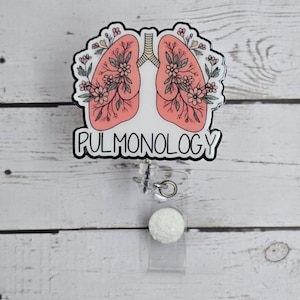 Puede incluir: Un dise&ntilde;o floral blanco y rosa de pulmones con la palabra "PULMONOLOGY" en texto negro. El dise&ntilde;o est&aacute; en un carrete de credencial transparente con una bola de purpurina blanca.