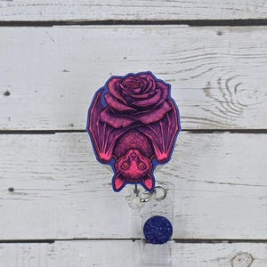 May include: A pink and purple bat with a pink rose hanging from a blue and clear retractable badge reel.