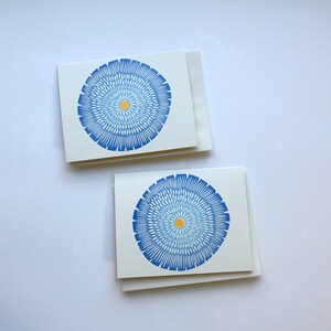 Op de afbeelding: Twee blanco wenskaarten met blauwe en gele cirkelvormige ontwerpen. De kaarten zijn dubbelgevouwen en liggen op een wit oppervlak.