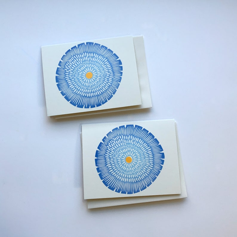 Op de afbeelding: Twee blanco wenskaarten met blauwe en gele cirkelvormige ontwerpen. De kaarten zijn dubbelgevouwen en liggen op een wit oppervlak.