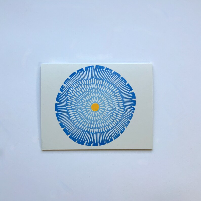 Op de afbeelding: Een blauw en wit cirkelvormig ontwerp met een geel centrum. Het ontwerp doet denken aan een bloem of een mandala.