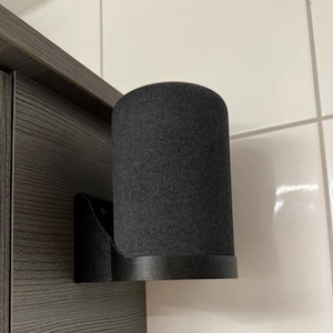 Op de afbeelding: Een zwarte wandbeugel voor een slimme speaker. De beugel is gemaakt van plastic en heeft een gebogen ontwerp om de speaker veilig vast te houden. De speaker is niet inbegrepen.