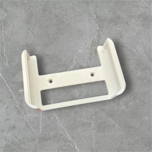 以下が含まれることがあります： 白いプラスチック製の壁掛けで、取り付け用のネジ穴が2つあります。マウントには、デバイスを保持するための長方形の開口部があります。