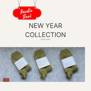 Op de afbeelding: Olijfgroene sokken uit de New Year Collection, elk met een wit label. De afbeelding bevat een rood "Bundle Deal"-label. De labels op de sokken luiden "Wishing you a year filled with love, warmth, and cozy socks."