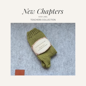 May include: A green knitted sock with a cream-colored label. The label has text that reads, "You helped me turn the page. Because of you, new chapters feel possible." The sock is part of the "Teachers Collection."