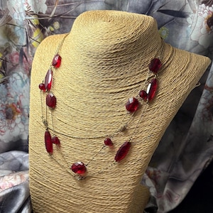 May include: A multi-strand gold-tone chain necklace featuring faceted, translucent red beads in various shapes and sizes. The delicate metallic chains are interspersed with small, textured gold-coloured metal accents, creating a layered appearance.