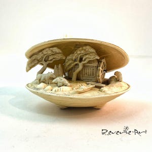 Könnte beinhalten: Eine detaillierte Elfenbeinschnitzerei einer japanischen Dorfszene in einer Muschelschale. Die Szene umfasst ein kleines Haus, Bäume, ein Wasserrad und Figuren von Menschen und Tieren.