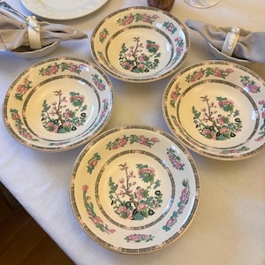 Puede incluir: Cuatro cuencos de cerámica color crema con diseños florales y de árboles. Cada cuenco presenta un motivo central de árbol con flores rosas y verdes, rodeado por un borde decorativo de flores rosas y un patrón geométrico gris. Los cuencos tienen un borde dorado.