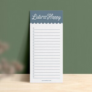 Pode incluir: Um bloco de notas azul com o texto "Lists Make Me Happy" no topo. O bloco de notas tem uma borda festonada e um fundo branco com linhas e caixas de sele&ccedil;&atilde;o.