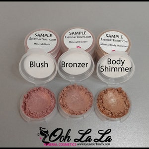 May include: A collection of mineral cosmetics samples, including blush, bronzer, and body shimmer. Each sample is in a small, clear container with a white lid. The blush is a dusty rose color, the bronzer is a medium brown, and the body shimmer is a light bronze. The text "Blush", "Bronzer", and "Body Shimmer" are printed on the lids.