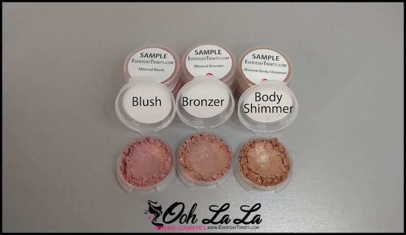 May include: A collection of mineral cosmetics samples, including blush, bronzer, and body shimmer. Each sample is in a small, clear container with a white lid. The blush is a dusty rose color, the bronzer is a medium brown, and the body shimmer is a light bronze. The text "Blush", "Bronzer", and "Body Shimmer" are printed on the lids.