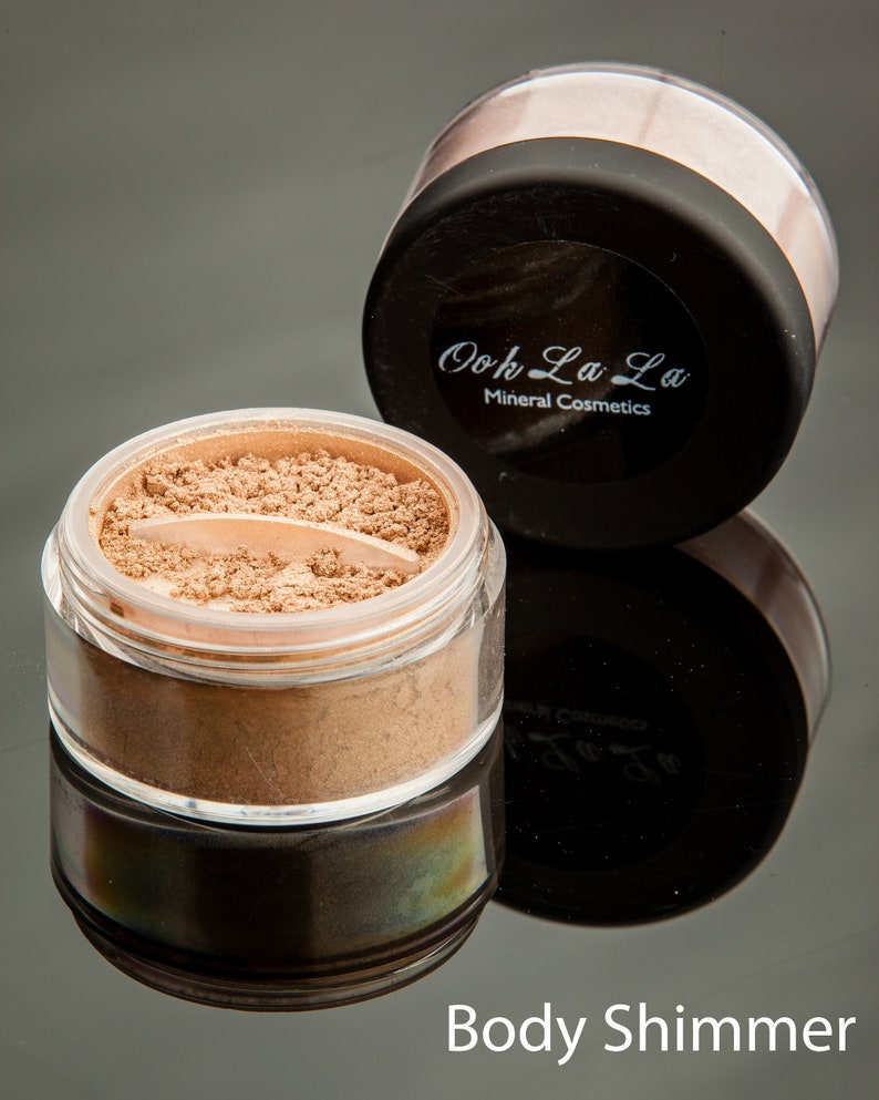 May include: Two jars of body shimmer. One jar is open, revealing a light brown powder. The other jar is closed with a black lid and the text "Ooh La La Mineral Cosmetics". The text "Body Shimmer" is at the bottom.