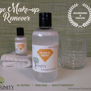May include: Two bottles of clear eye makeup remover with a white label that says "100% Natural Eye Make-up Remover Trinity EverydayTrinity.com". The smaller bottle is 2 oz and the larger bottle is 9.2 oz. The bottles are on a white surface with a white knitted washcloth and a clear glass.