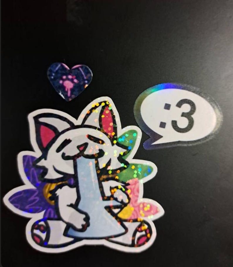 May include: A holographic sticker featuring a white cat character holding a light blue water pipe, surrounded by colorful floral shapes. Above the cat is a small heart-shaped sticker, and to the right is a speech bubble sticker with the text :3.