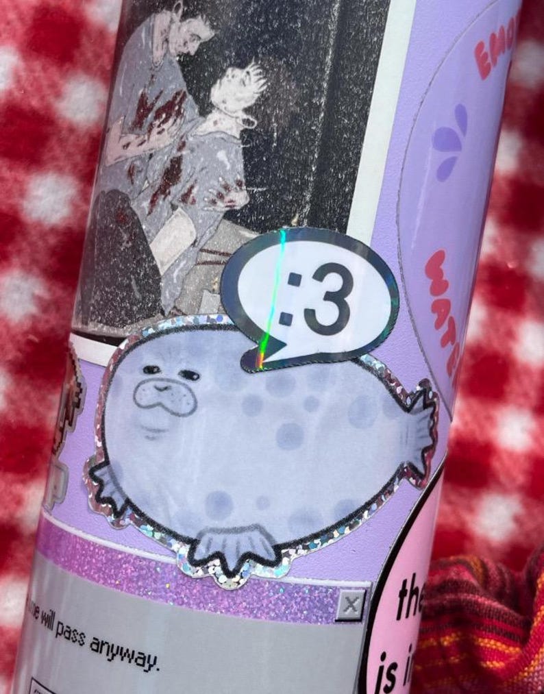 May include: A cylindrical tumbler decorated with various stickers, including a light purple seal with a holographic border and a speech bubble containing the text :3, a black and white illustration of two figures, and text reading the will pass anyway.