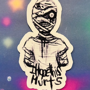Puede incluir: Una pegatina con una ilustración en blanco y negro de una figura similar a una momia con vendas y la boca abierta. El texto "I Hope this Hurts" está escrito en negro debajo.