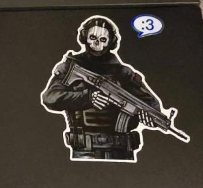 May include: A sticker featuring a character wearing a skull mask and tactical gear, holding a rifle with skeletal hands. The character is dressed in black and grey, and a small blue speech bubble with the text :3 is positioned above the right shoulder.