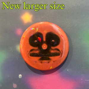 May include: A round button with a red background and a black and white image of a face with a large mouth and a small nose. The button has a glittery finish.