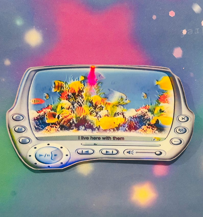 May include: A white and blue digital picture frame with a screen showing a colorful underwater scene with fish and coral. The frame has buttons for controlling playback and the text "I live here with them" is displayed on the screen.