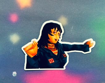 Puede incluir: Una pegatina con un personaje de dibujos animados con cabello negro, que lleva una chaqueta azul con un parche de corazón rojo y una camisa a rayas. El personaje sonríe y tiene los brazos extendidos.