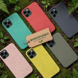 Puede incluir: Seis fundas para smartphone en color verde azulado, rojo, gris oscuro, rosa claro, amarillo y verde oliva, cada una con un recorte para cámara de triple lente. Una etiqueta rectangular color canela tiene el texto BIODEGRADABLE Eco-Friendly Material.