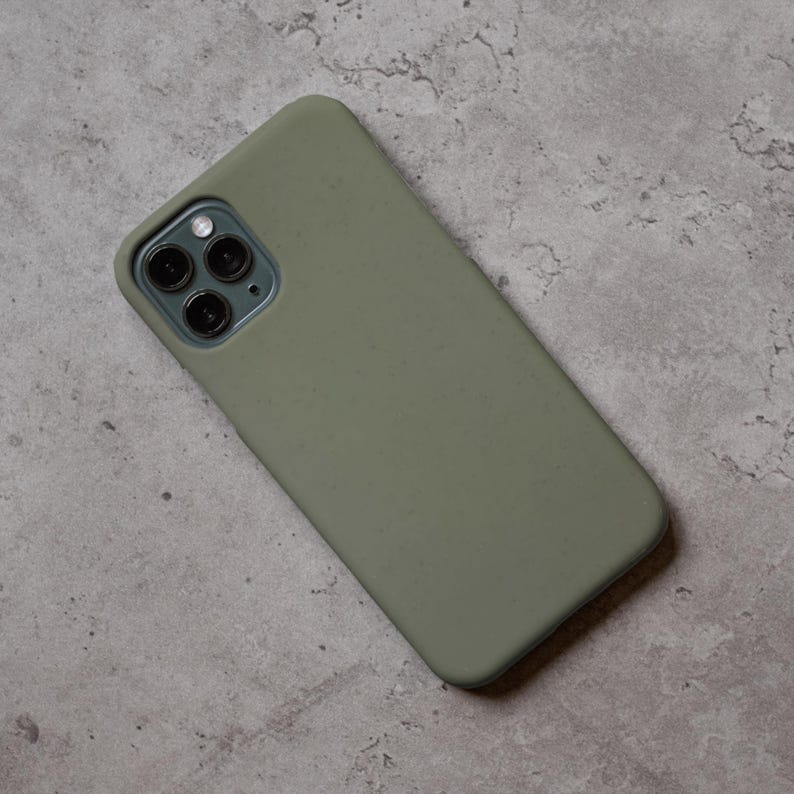 Puede incluir: Funda de tel&eacute;fono verde oliva con acabado mate. La funda est&aacute; dise&ntilde;ada para adaptarse a un tel&eacute;fono inteligente con una c&aacute;mara de triple lente. La funda del tel&eacute;fono est&aacute; sobre una superficie gris texturizada.