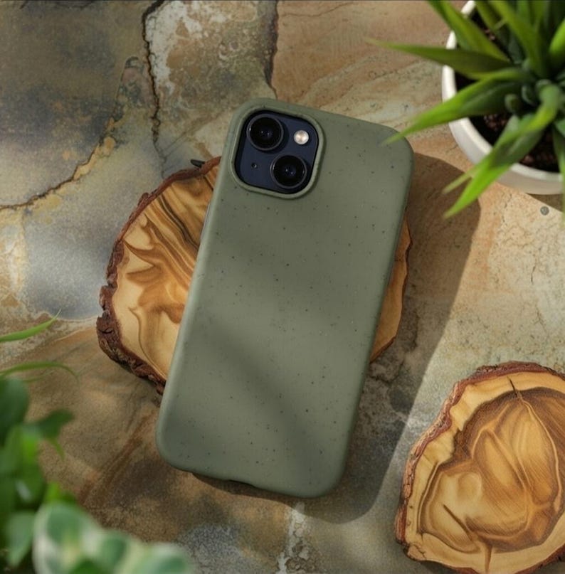 May include: A matte olive green smartphone case with a subtle speckled texture. The case features a raised rectangular camera cutout at the top left, housing two circular camera lenses and a small flash, designed for a modern mobile device.