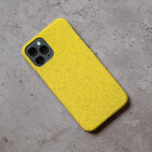 Puede incluir: Una funda de tel&eacute;fono amarilla moteada con un recorte para la c&aacute;mara. La funda est&aacute; hecha de un material texturizado y est&aacute; dise&ntilde;ada para adaptarse a un tel&eacute;fono inteligente. La funda del tel&eacute;fono es de color amarillo brillante.