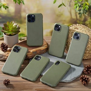 May include: A collection of six olive green smartphone cases with varying camera cutout configurations. The cases feature a smooth, matte finish and are arranged on a wooden surface alongside a small potted succulent and pinecones.