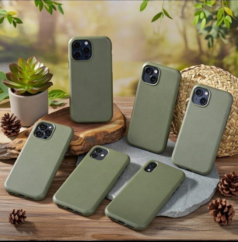 May include: A collection of six olive green smartphone cases with varying camera cutout configurations. The cases feature a smooth, matte finish and are arranged on a wooden surface alongside a small potted succulent and pinecones.