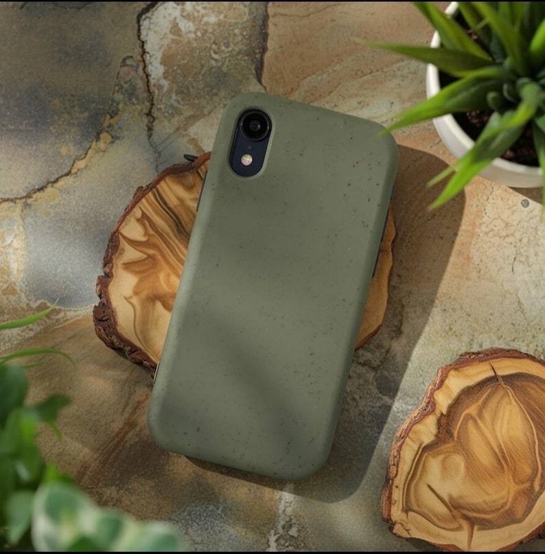 May include: A matte olive green smartphone case with a speckled texture. The case features a single circular camera cutout in the upper left corner with a black lens housing and a small circular flash opening positioned directly below the lens.