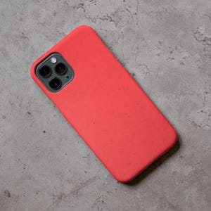 Puede incluir: Una funda de tel&eacute;fono de color coral con una superficie texturizada. La funda tiene un recorte para la c&aacute;mara con tres lentes y un flash. La funda est&aacute; dise&ntilde;ada para un tel&eacute;fono inteligente.