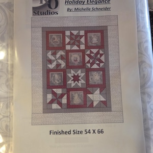Könnte beinhalten: Ein Quiltmuster mit dem Titel "Holiday Elegance" von Michelle Schneider. Das Design zeigt ein Raster aus Quadraten mit roten und weißen Stern- und Engelmotiven. Fertige Größe: 137 x 168 cm.