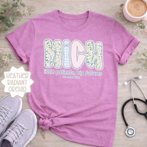 May include: A lilac t-shirt with the word "NICU" in a floral design, and the text "little patients, big futures" and "Jeremiah 29:11". A stethoscope and a pair of trainers are also visible.