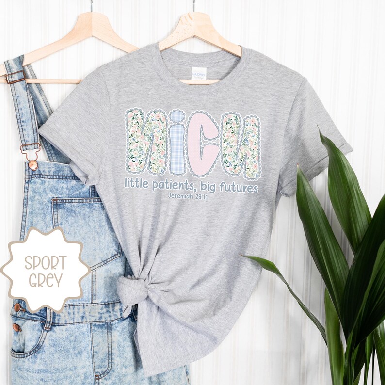 May include: Sport grey t-shirt featuring the word "NICU" in a floral and gingham design, with the text "little patients, big futures" and the Bible verse Jeremiah 29:11. The shirt is displayed on a wooden hanger.