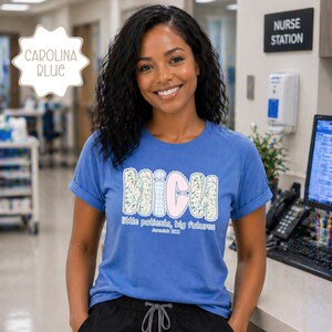 May include: A Carolina blue t-shirt with rolled sleeves. The shirt displays the letters "MICU" in a floral and gingham design, with the words "Little patients, big futures" underneath. The shirt is worn by a smiling person.