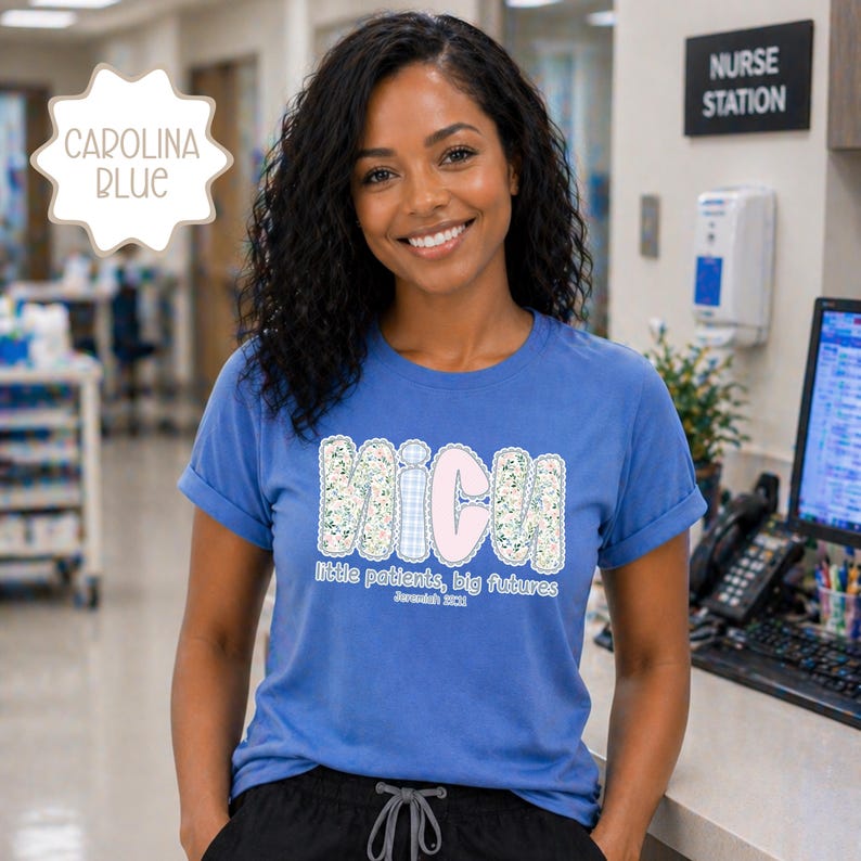May include: A Carolina blue t-shirt with rolled sleeves. The shirt displays the letters "MICU" in a floral and gingham design, with the words "Little patients, big futures" underneath. The shirt is worn by a smiling person.
