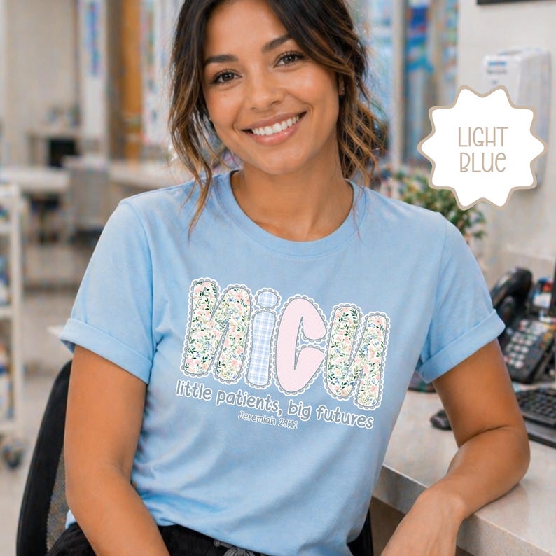 May include: Pale blue t-shirt featuring the word "NICU" in a floral and gingham design, with the text "little patients, big futures" and "Jeremiah 29:11". The shirt has short sleeves.