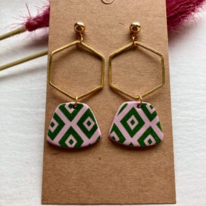 May include: A pair of gold hexagon earrings with pink and green geometric patterned charms.