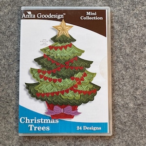 May include: A clear plastic case featuring a Christmas tree design. The tree is green with red heart-shaped ornaments and a gold star. The case reads "Anita Goodesign" and "Christmas Trees, 24 Designs."