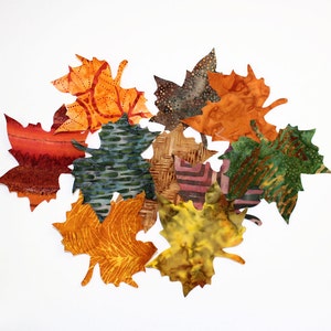 May include: A collection of fabric maple leaves in various colors and patterns, including orange, red, green, brown, and yellow.
