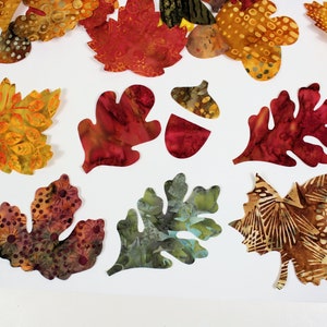 May include: Assortment of fabric leaves in various colors and patterns, including red, orange, yellow, green, and brown. The leaves are cut out and ready to be used for crafting projects.