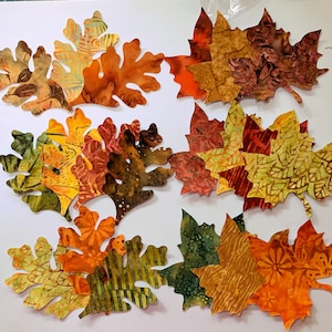 May include: A collection of 10 fabric leaves in various shades of orange, brown, and green. The leaves are cut from fabric with a batik pattern and are perfect for crafting projects.