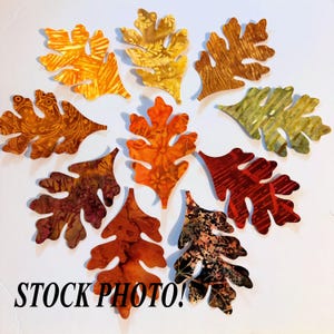 May include: Ten fabric oak leaves in various autumnal colors and patterns, including orange, brown, red, and green. The leaves are arranged in a circle on a white background. "STOCK PHOTO!" is written in black text at the bottom of the image.