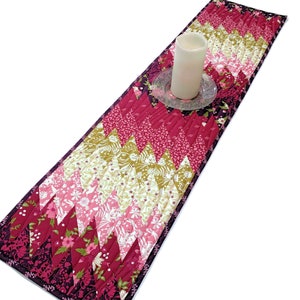 May include: A quilted table runner with a chevron pattern in shades of burgundy, pink, and gold. The runner is approximately 14 inches wide and 72 inches long.