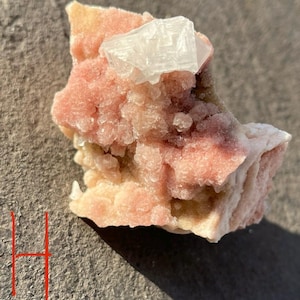 May include: A pink and white crystal cluster with a large, clear, white crystal on top. The crystal cluster is rough and has a natural, organic shape.